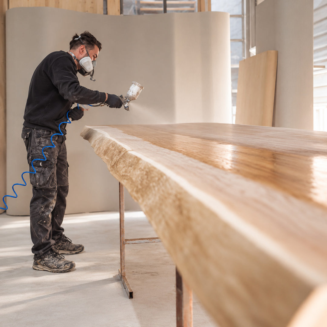 spritzen-holztisch.jpg	Verarbeiter mit Atemschutz und Handschuhen spritzlackiert eine massive Holztischplatte