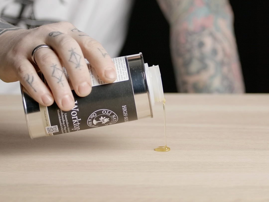 OLI NATURA Worktop-Oil wird aus einer Metalldose auf eine Holzoberfläche gegossen