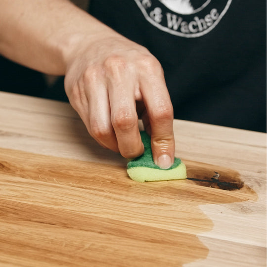 Eine rohe Eichenplatte wird mit einem Schwamm und verdünntem OLI NATURA® PreOilCleaner nebelfeucht abgewischt